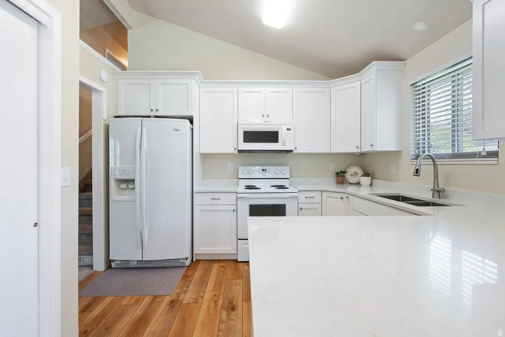 Kitchen featuring white cabinetry, light-colored countertops, stainless steel sink with pull-down faucet, and wood-finish flooring