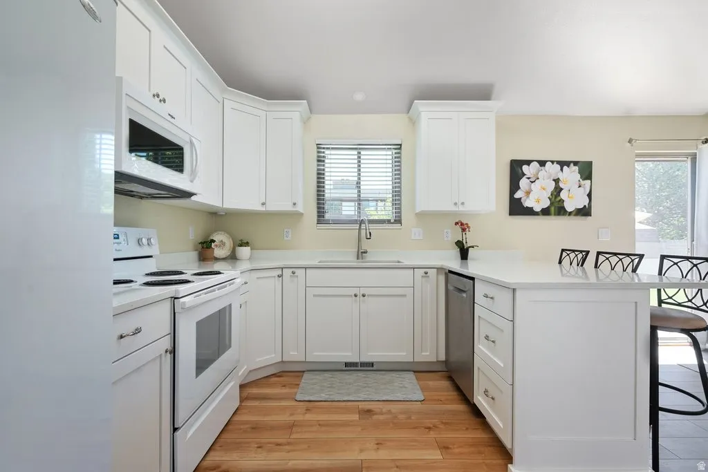 Modern kitchen featuring white cabinetry, light-toned countertops, a built-in microwave, a flat-top stove, and wood-finish flooring