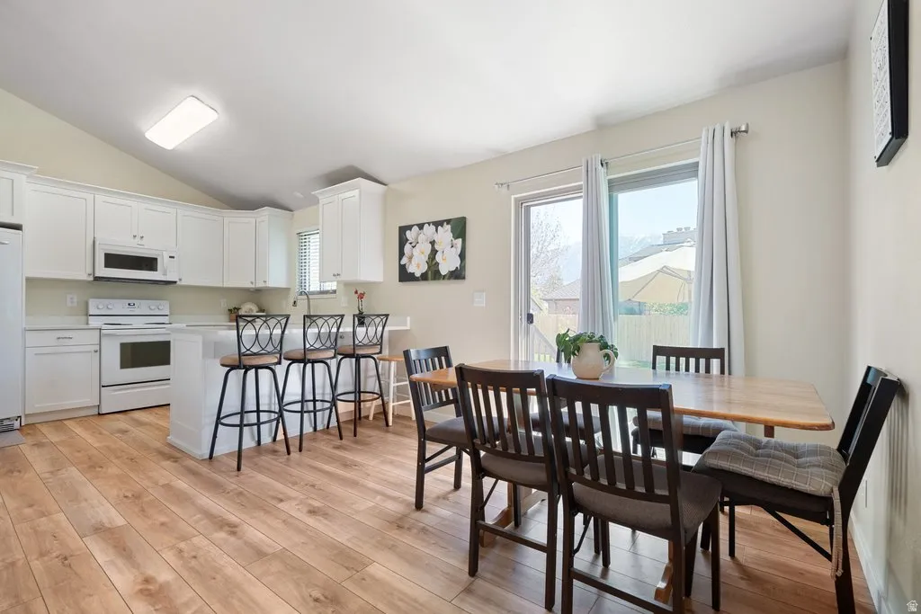 Open-concept kitchen and dining area featuring wood-finish flooring, white cabinetry, a kitchen island with seating, white appliances, and a sliding glass door