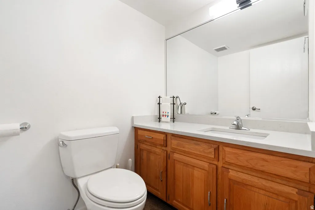 Bathroom featuring a light wood-finish vanity with a light countertop, an integrated sink with chrome faucet, a large wall-mounted mirror, and a toilet