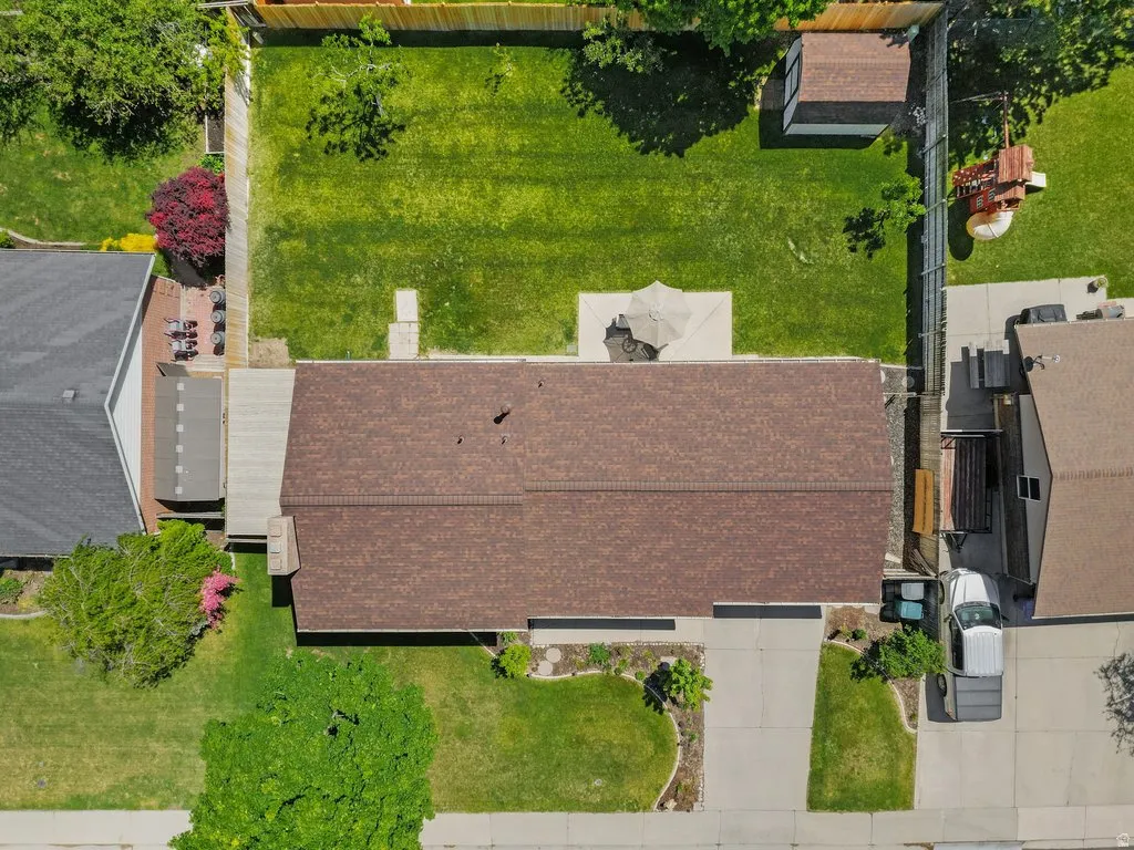 Expansive backyard featuring a manicured lawn, established trees, a concrete patio, and a storage shed