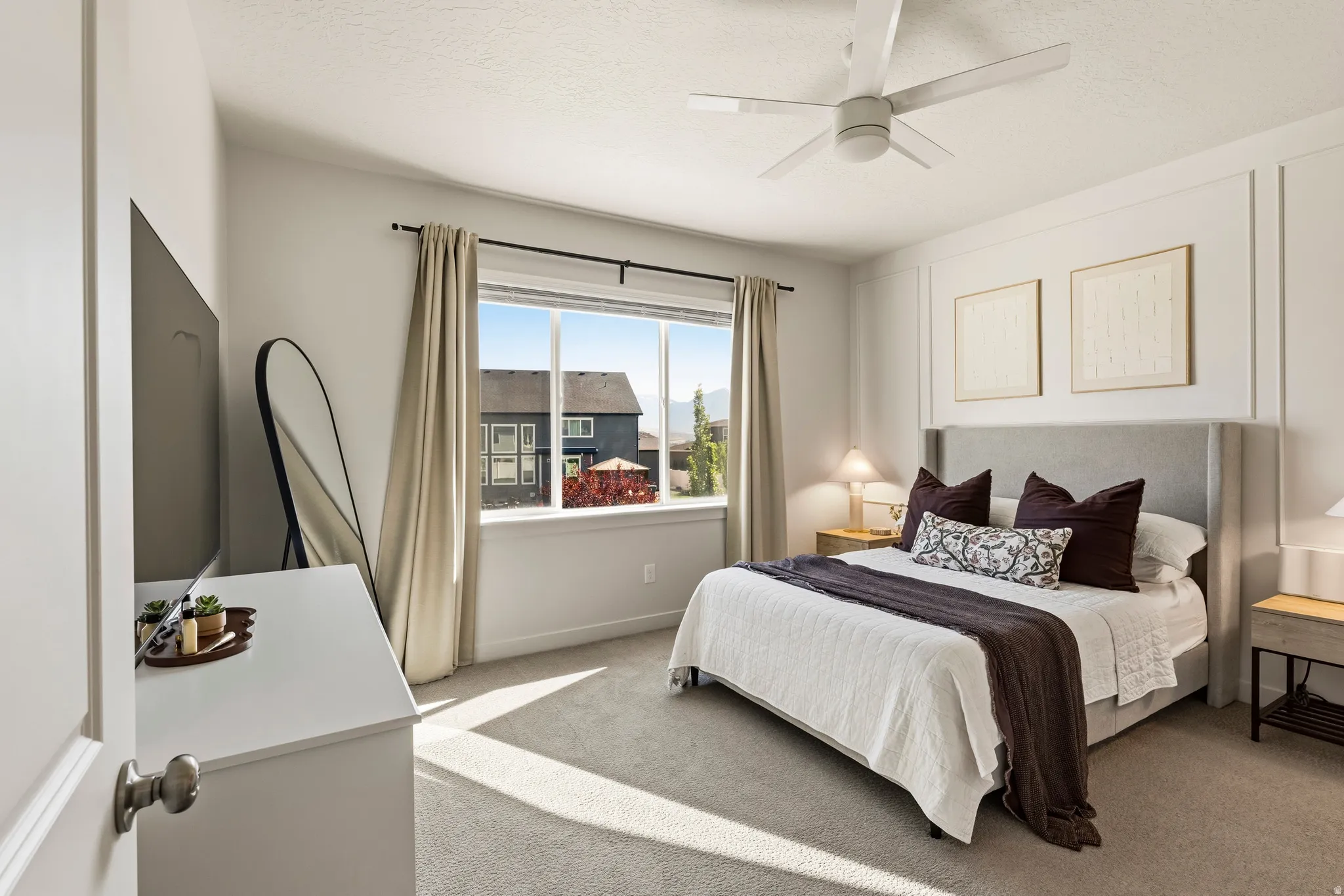 Carpeted bedroom featuring a large window, ceiling fan, and wall paneling