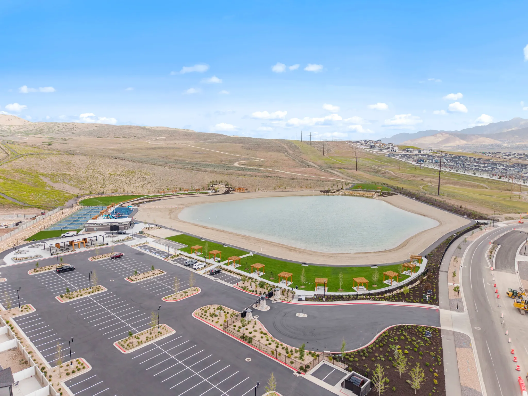Expansive community recreation area featuring a large lake with a sandy shoreline, manicured green spaces, and multiple shade structures