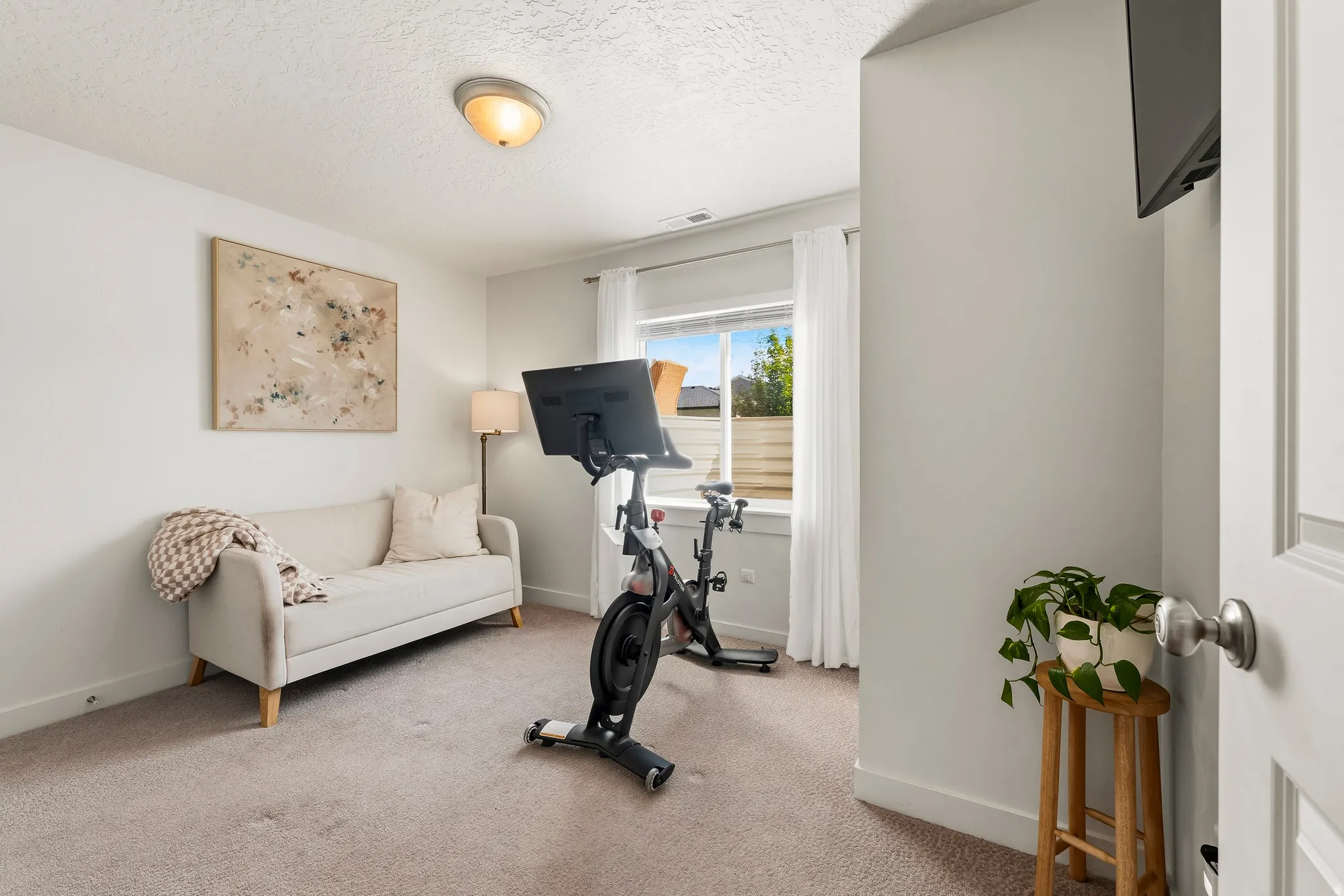 Carpeted interior room with white walls and a large window featuring white curtains