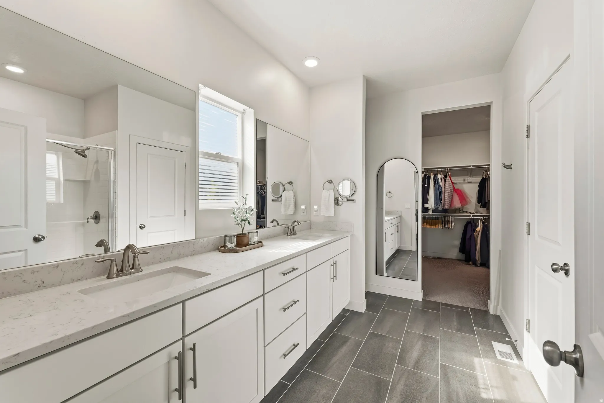 Spacious bathroom featuring a dual vanity with light-toned countertops, white cabinetry, and a large mirror