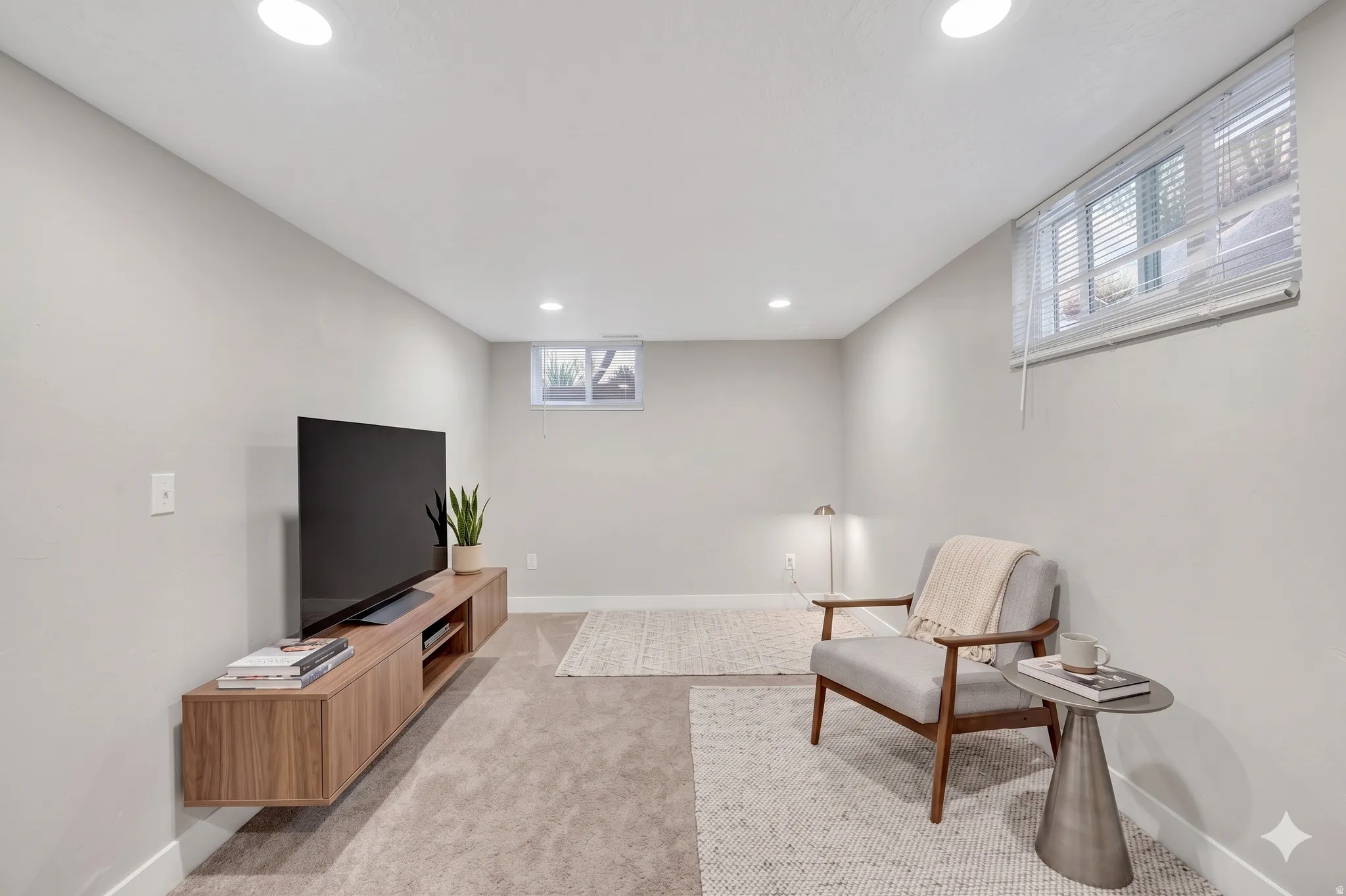 Recessed ceiling lighting illuminates this versatile space featuring light gray walls, plush carpet, and a built-in wood-finish media console