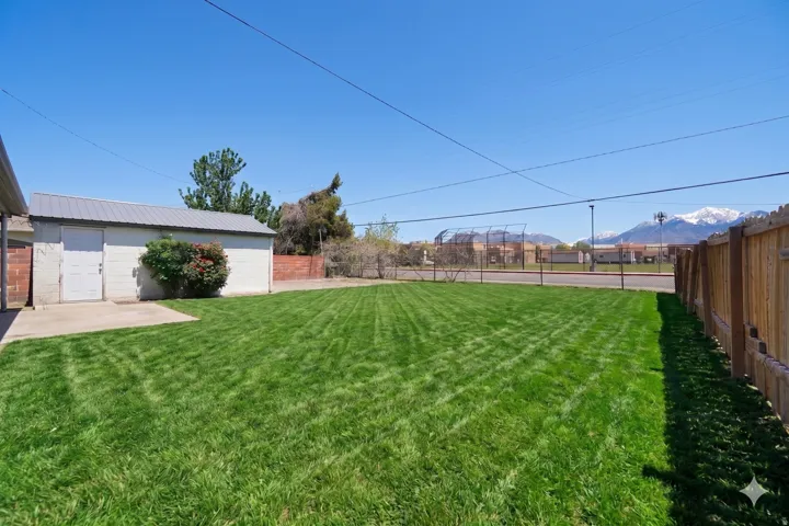 Expansive backyard featuring a manicured lawn, a detached utility building with a metal roof, and a concrete patio
