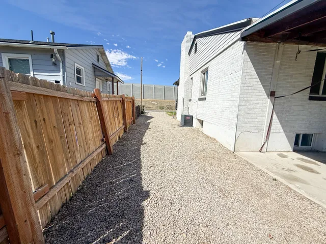 Gravel walkway alongside a wood privacy fence, leading to a light-colored brick exterior with a lower-level window