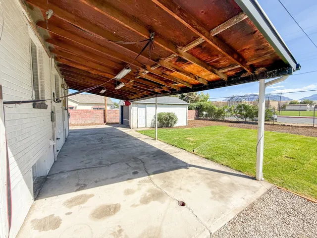 Covered concrete patio with exposed wood ceiling, white brick exterior, and adjacent gravel area