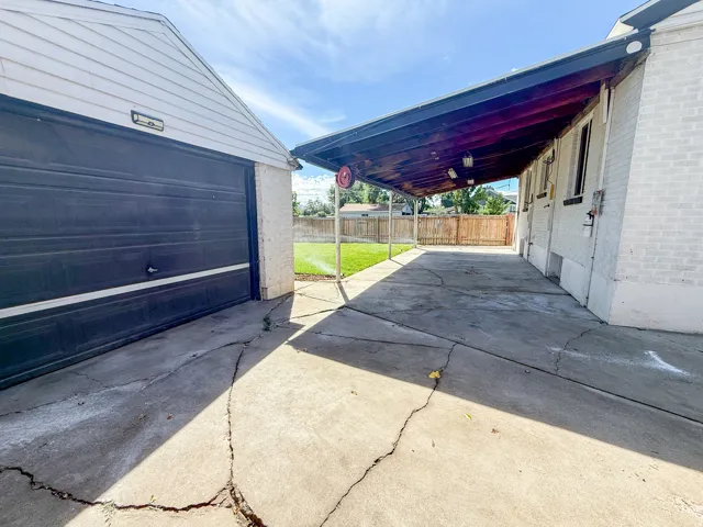 Detached garage with a roll-up door, covered carport with exposed wood beams, and a fenced backyard