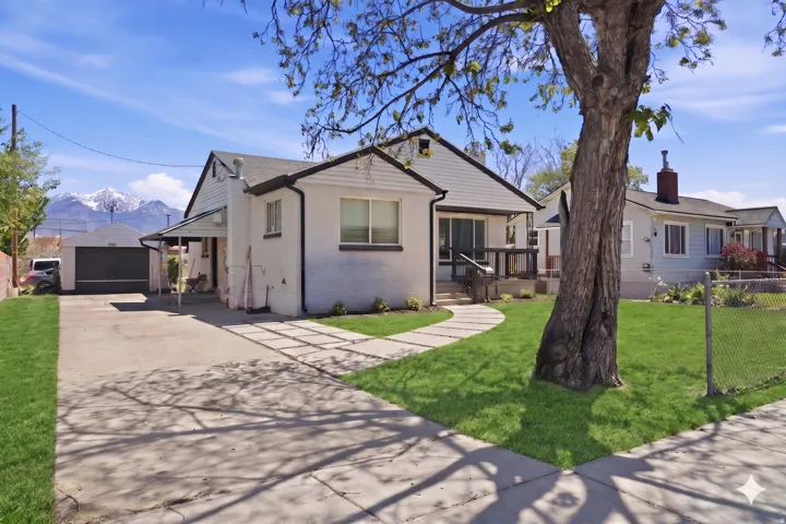 White exterior residence featuring a front yard with manicured lawn, a paved driveway, and a detached garage