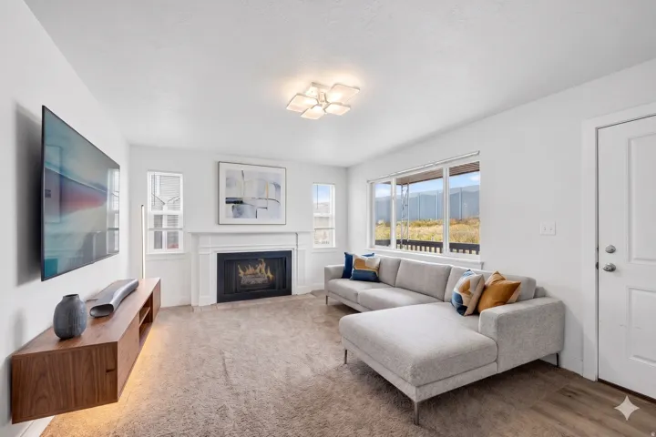 Spacious living area featuring a fireplace with a white mantel, large windows, a decorative ceiling light fixture, and wood-finish flooring