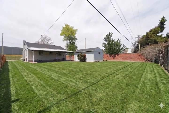 Expansive rear yard featuring a wide lawn area, a detached storage shed, and a covered patio area