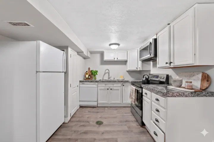 Kitchen featuring wood-finish flooring, white cabinetry with dark hardware, speckled countertops, and a full suite of white and stainless steel appliances