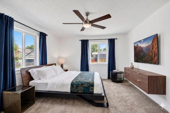 Bright room featuring two windows with dark blue drapes, a ceiling fan, and carpeted flooring