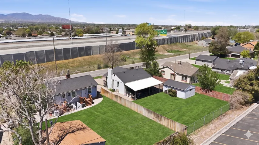 Expansive green lawn with a chain-link fence, mature trees, and an open carport structure