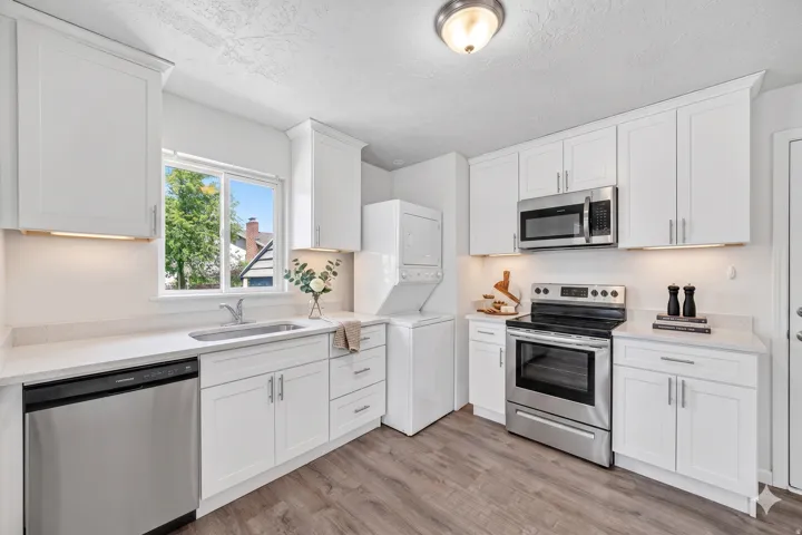 Kitchen featuring white shaker cabinetry, stainless steel appliances, light-toned countertops, and wood-finish flooring
