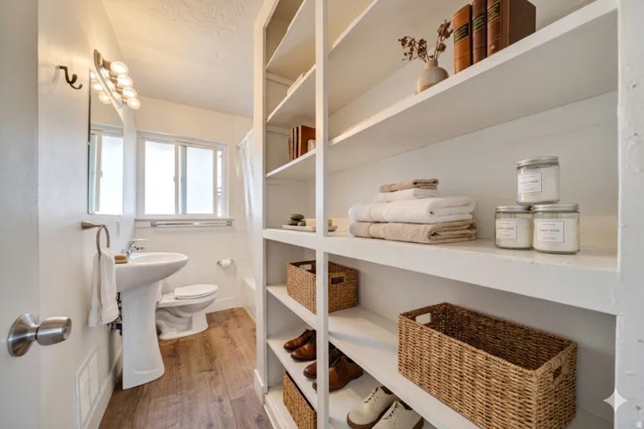 Full bathroom with pedestal sink, toilet, and wood-finish flooring