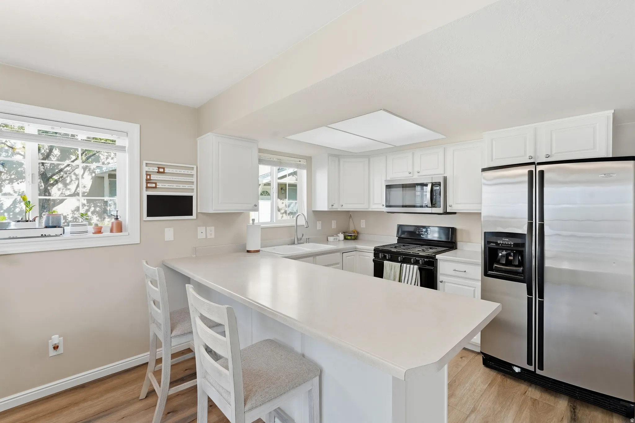 Kitchen featuring white cabinetry, light-toned countertops, wood-finish flooring, stainless steel appliances, and an island with bar seating