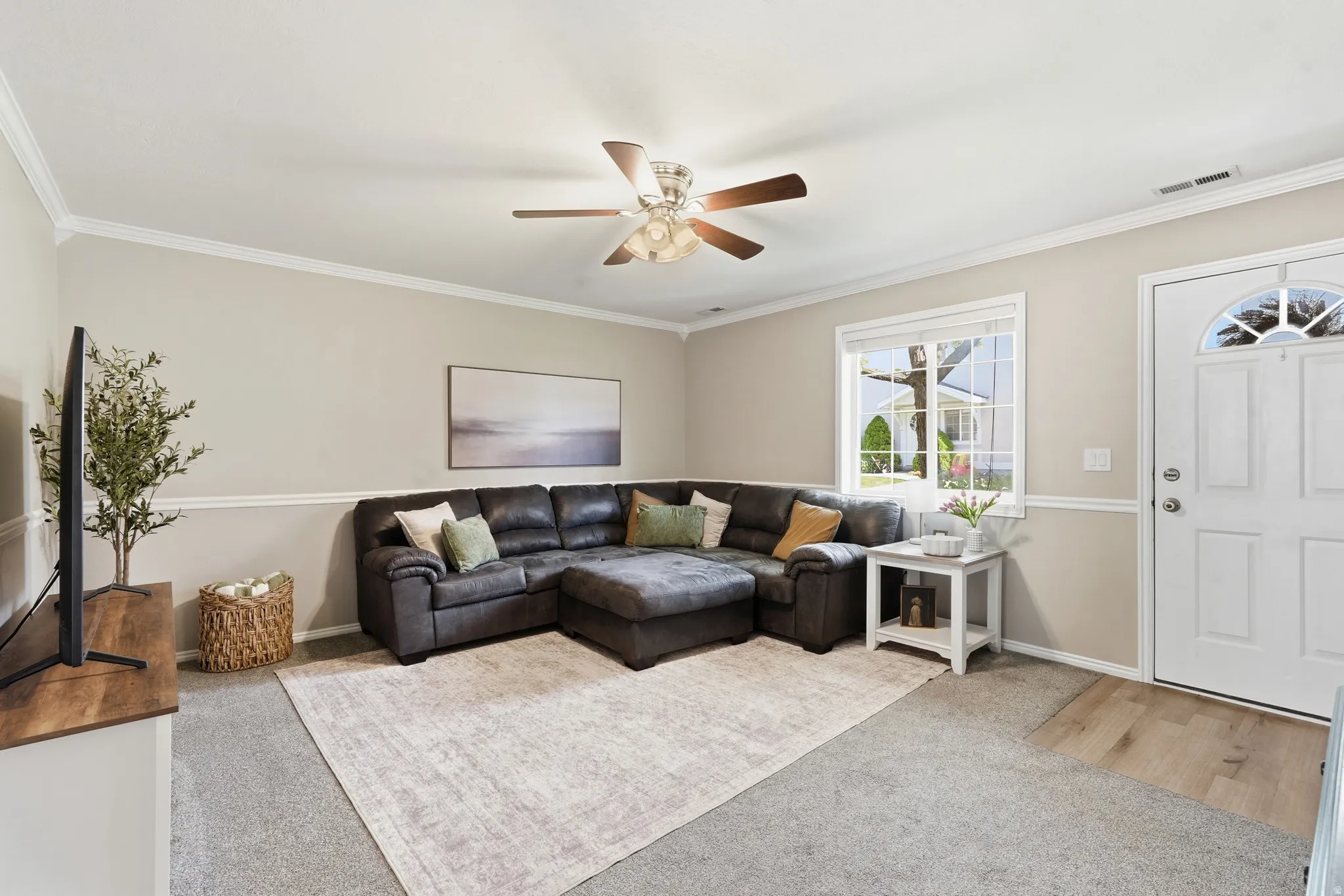 Living room featuring crown molding, two-tone wall treatment, a ceiling fan with light fixture, a window with exterior views, and a front entry door with an arched glass insert