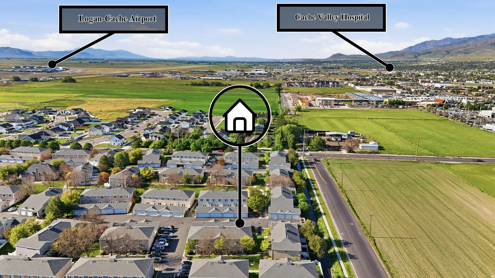 Aerial perspective showcasing a residential community with varied architectural styles, bordered by expansive green fields and distant mountains