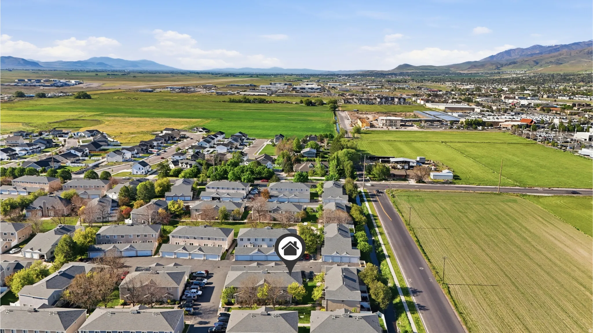 Residential community featuring multiple townhome structures and single-family homes, surrounded by expansive green fields and distant mountains