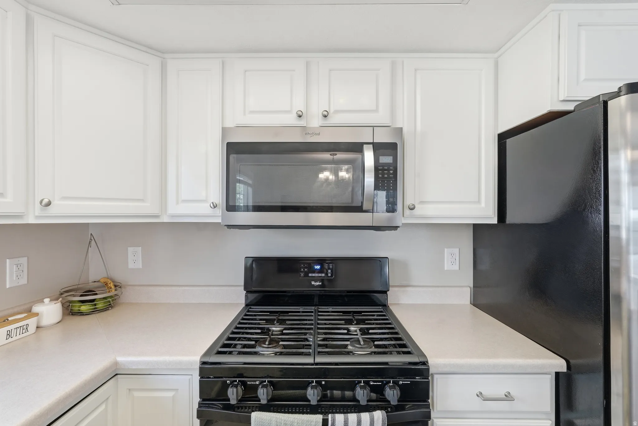 Kitchen featuring white cabinetry, light-toned countertops, a black gas range, and a stainless steel microwave