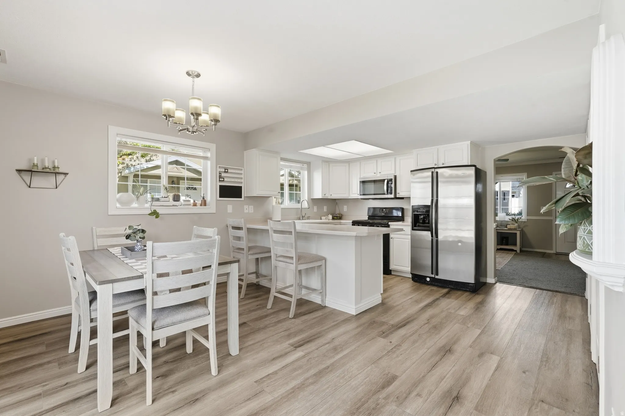 Open concept kitchen and dining area featuring wood-finish flooring, white cabinetry, stainless steel appliances, a kitchen island with bar seating, and a dining area with a chandelier