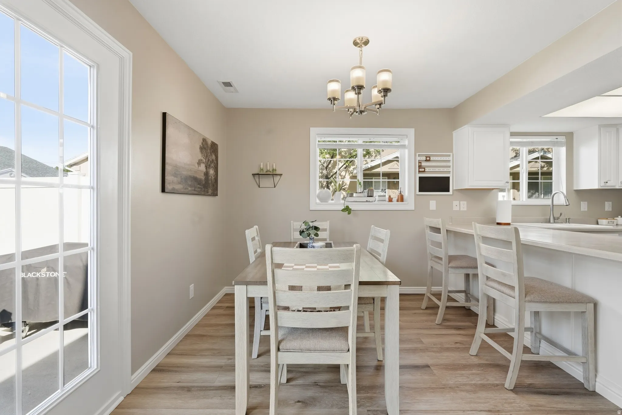 Open-concept dining area featuring wood-finish flooring, a contemporary chandelier, and direct access to the exterior through a glass-paned door