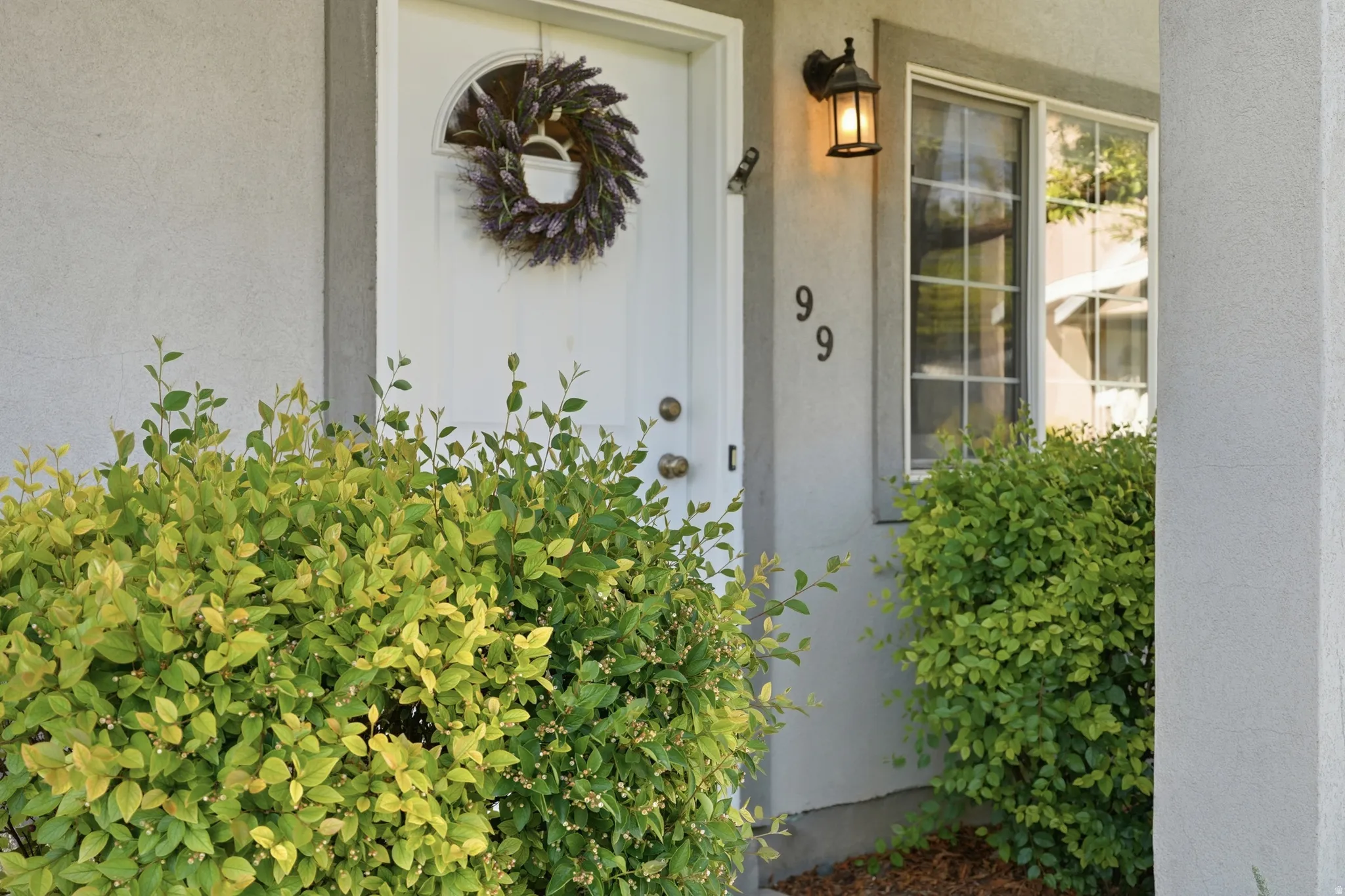 Exterior featuring a white entry door with an arched window, a grid-pattern window, and an outdoor wall lantern