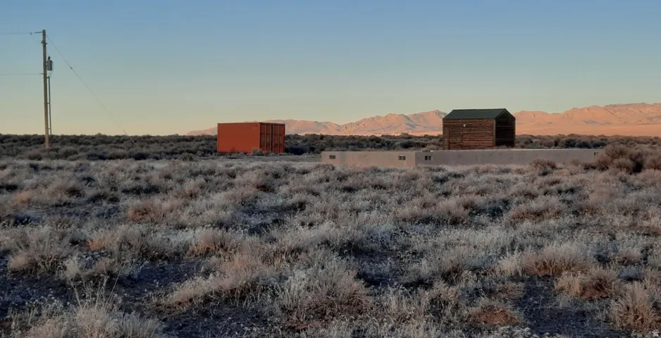 Expansive desert landscape featuring a rustic wooden structure and a red storage container, with a distant mountain range backdrop