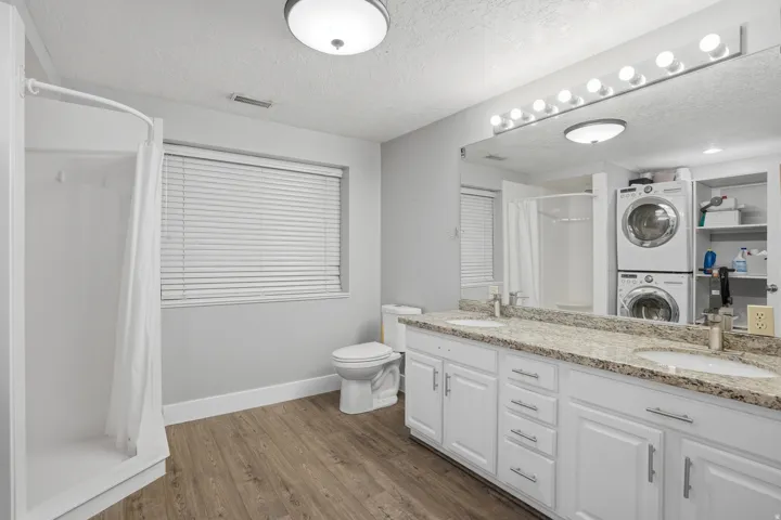 Bathroom featuring a dual vanity with granite-finish countertop, wood-finish flooring, and a white shower stall