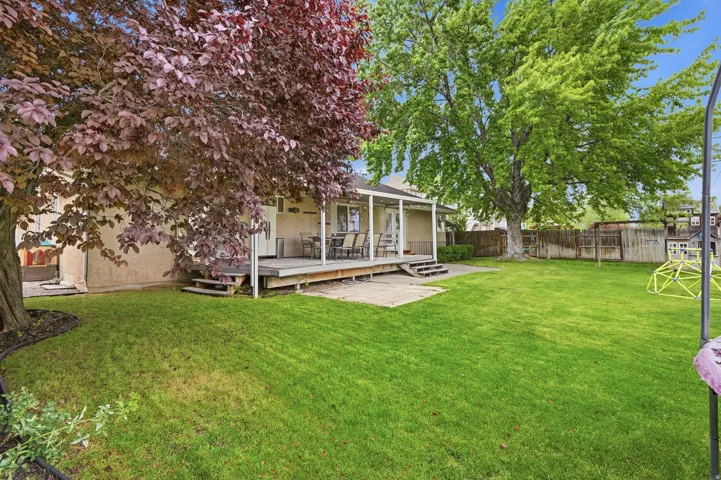 Spacious green lawn featuring a covered wood deck, mature trees, and a privacy fence