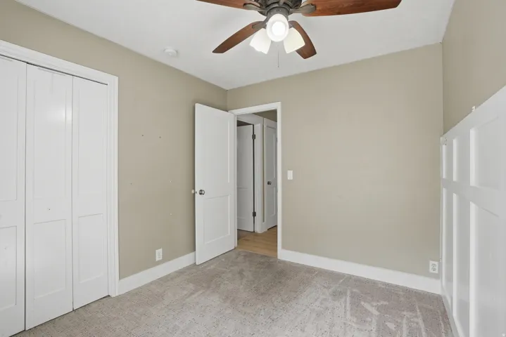 Carpeted room featuring a ceiling fan with light fixture, white baseboards, and a white paneled closet