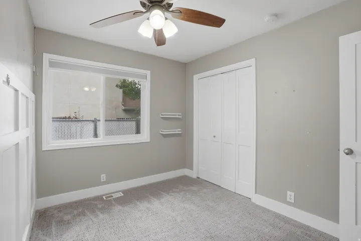 Carpeted room featuring a ceiling fan with integrated lighting, a white-framed window, and a bi-fold closet door