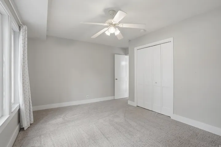 Carpeted room with light gray walls, a white ceiling fan with integrated lighting, and white bi-fold closet doors