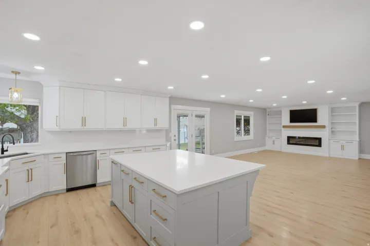 Spacious kitchen with a large island, white cabinetry, integrated stainless steel appliances, and wood-finish flooring