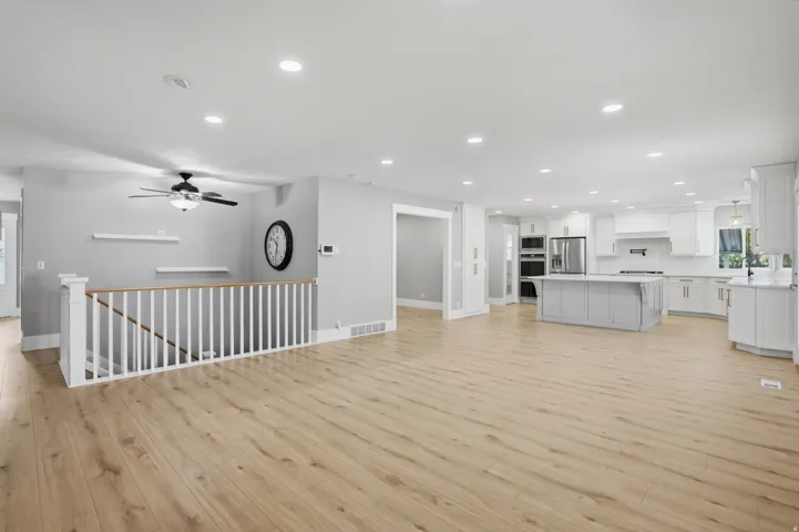 Open-concept main level featuring light wood-finish flooring, recessed lighting, and a white balustrade staircase