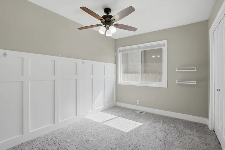 Room featuring board and batten wall paneling, a ceiling fan with integrated lighting, and a single window with blinds