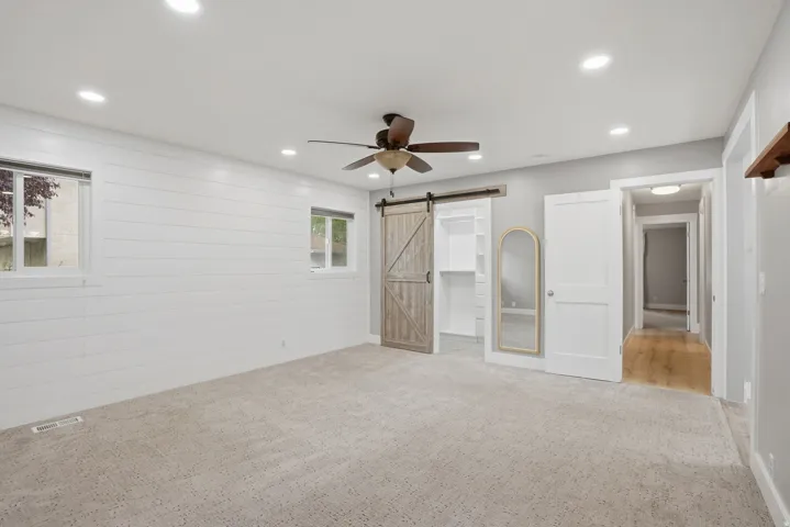 Spacious room featuring light gray carpeting, recessed lighting, and a dark-toned ceiling fan