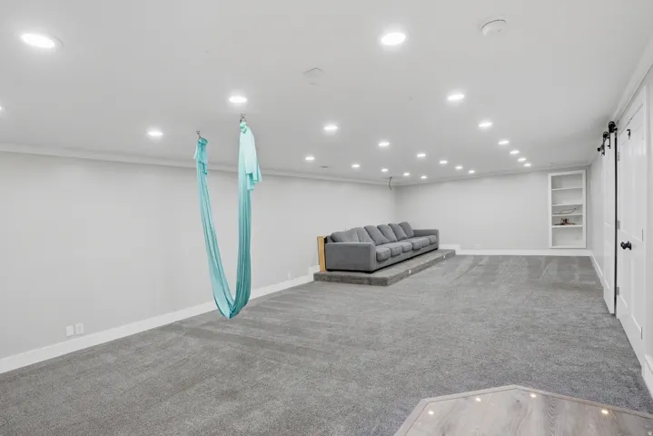 Spacious recreation room featuring recessed lighting, light gray carpeting, and a built-in bookshelf