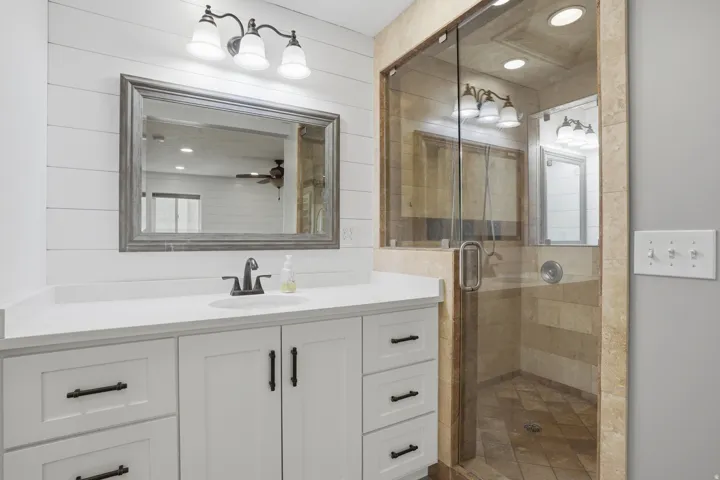 Contemporary bathroom featuring a white shaker-style vanity with a single basin, a gray-framed mirror, and a three-light fixture