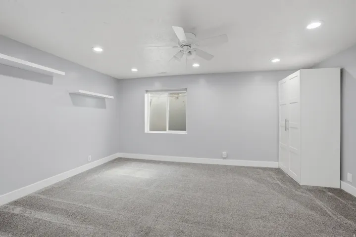 Spacious room featuring plush gray carpeting, recessed ceiling lighting, a white ceiling fan, and a built-in white storage cabinet