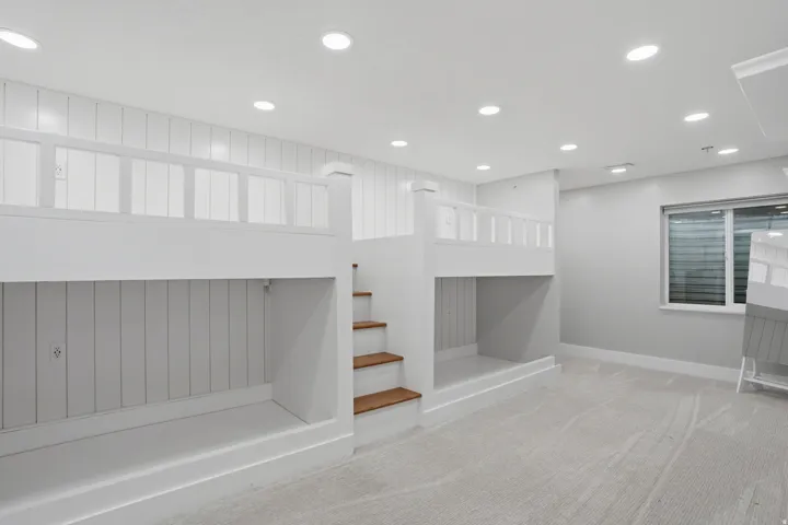 Custom-built bunk beds with integrated wooden stairs, white shiplap wall paneling, recessed lighting, wall-to-wall carpeting, and a window with horizontal blinds