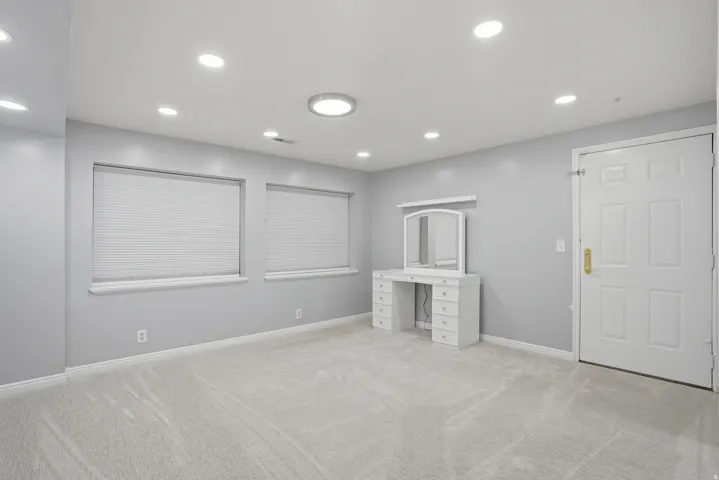Spacious room featuring light gray walls, plush carpeting, recessed lighting, and two windows with blinds