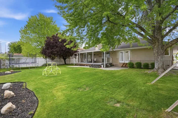 Expansive backyard featuring a manicured lawn, mature trees, a concrete patio, and a covered wood deck