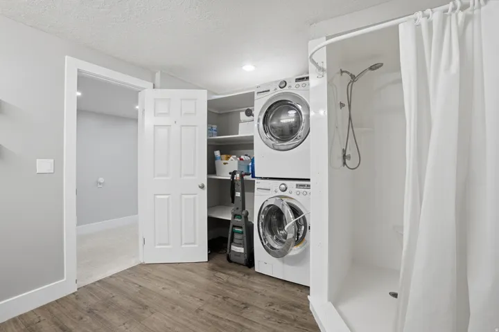 Laundry area featuring stacked appliances, built-in shelving, and wood-finish flooring