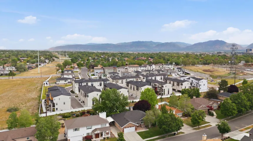 Aerial perspective showcasing a community of multi-story residences with dark roofs and light-colored exteriors, interspersed with mature trees