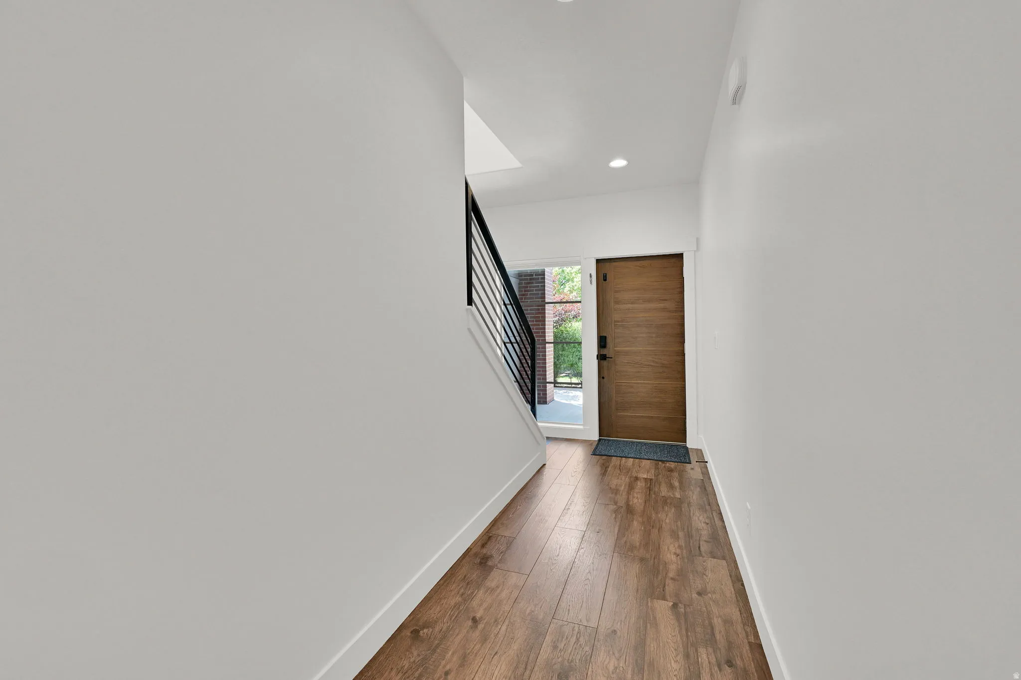 Entryway featuring rich wood-finish flooring, a modern wood-paneled door with frosted glass sidelight, and a minimalist black metal staircase railing