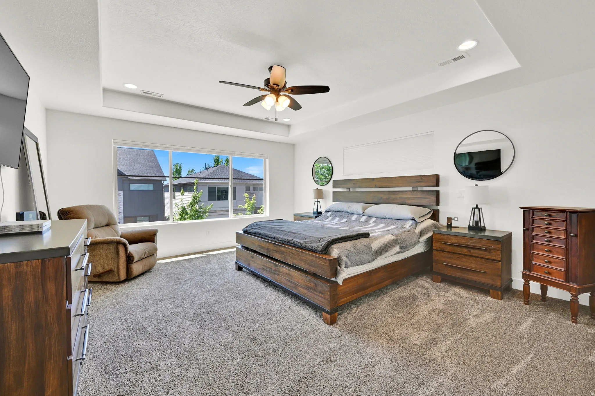 Spacious bedroom with a tray ceiling and recessed lighting, featuring a wide window, ceiling fan, and carpeted flooring
